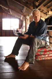 Jeremy Wade in North Thailand sat in an attic with his socks and shoes off holding his diary.
