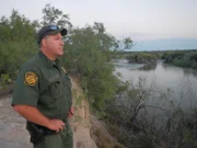 Roma, Texas, USA: David Maibaum in uniform standing above the Rio Grande River and looking over to the other side - profile of right side.