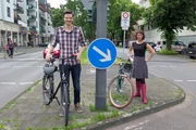 Die "Xenius"-Moderatoren Emilie und Adrian mit ihren Fahrrädern auf einer Verkehrsinsel.