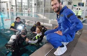Unter Wasser im Weltraumanzug: "X:enius"-Moderatorin Dörthe (Mi.) übt bei der ESA in Köln. Co-Moderator Pierre (re.) beobachtet das Ganze aus sicherer Entfernung vom Beckenrand.