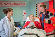 Annemarie (Saskia Schindler, M.) wird mit einer Rauchgasvergiftung ins EKH eingeliefert. Dr. Jasmin Jonas (Gerit Kling, l.) und Dr. Haase (Fabian Harloff, r.) kümmern sich um die Patientin.