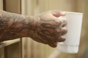 An inmate holding out cup out of bars.
