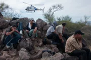 Nogales, AZ: Handcuffed men sitting on rocks, with a helicopter hovering in the background. Illegal immigrants and smugglers can be located with the use of helicopters.