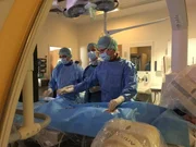 Mithilfe von Drähten und Schläuchen setzen Prof. Dr. med. Peter Ewert (r.) und Dr. med. Daniel Tanase (.) einem Mädchen eine neue Herzklappe ein. "pur+"-Moderator Eric Mayer (M.) ist bei dem Eingriff im Deutschen Herzzentrum München dabei.