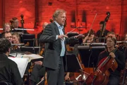 Thomas Hengelbrock moderiert vor dem Orchester stehend.