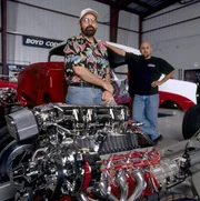 Boyd Coddington, L, standing behind the chrome-plated engine of the Junkyard Dog hot rod with Duane Mayer.