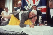 Der ungeschickte Lt. Frank Drebin (Leslie Nielsen, oben) versucht ein Attentat auf die britische Königin Elizabeth II. (Jeannette Charles, unten) zu vereiteln.