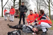 Notarzt Haase (Fabian Harloff, r.) und ein Kollege (Komparse) versorgen den Möbelpacker Hendrik Meffert (Tim Grobe, liegend), der in einem Park niedergeschlagen wurde. niedergeschlagen worden während Mattes (Matthias Schloo, l.) ermittelt, ob der Vorfall etwas mit dem Erbscheiftsstreit zu tun hat.