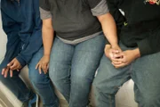 Brownsville, TX, USA: A mid-section shot of three apprehended people in a holding cell.