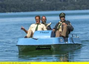 Hubert (Christian Tramitz, links) und Staller (Helmfried von Lüttichau, rechts) sitzen in einem Tretboot und fahren auf den See hinaus. Yazid (Hannes Ringelstetter) sitzt hinter ihnen in Tauchermontur. Er soll für Hubert und Staller testen, ob man mit einem Schlittschuh unter Wasser an einer Boje hängen bleiben kann.