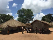 Shot of village huts with villagers standing outside them.