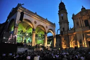 Blick auf den Odeonsplatz bei Nacht mit Bühne und Besuchern.
