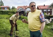 Polizeirat Girwidz (Michael Brandner, rechts) steht in Freizeitkleidung neben Riedl (Paul Sedlmeir) und beobachtet den Fortgang der Gartenarbeit. Dabei gibt er Riedl immer wieder Anweisungen.