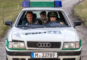 Johann Eberle (Joost Siedhoff, Mitte) wird von Hubert (Christian Tramitz, li.) und Staller (Helmfried von Lüttichau, re.) im Polizeiauto aufs Revier gefahren.