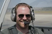 Josh Gates sitting in a P-51 Mustang with his headset on in Southern California.