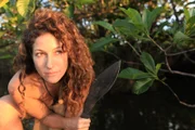 Gia, next to leaves, poses with a survival tool.