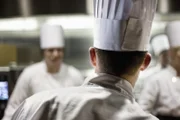 A closeup view from behind of a chef  wearing a toque hat in a commercial kitchen.