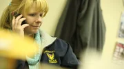 Jenny Luke at her desk in Police Jacket on phone.