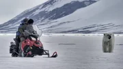 Joel Lambert and Trude Mostue on a skidoo passing a polar bear.