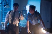 A cop and detective holding flashlights in the dark.