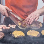 Chef, der die Rindfleischburger im Freien auf internationalem Lebensmittelfestivalereignis der offenen Küche macht. Street Food servierfertig auf einem Imbissstand.