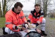 Notarzt Haase (Fabian Harloff, r.) und ein Kollege (Komparse) versorgen den Möbelpacker Hendrik Meffert (Tim Grobe, M.), der in einem Park niedergeschlagen wurde.