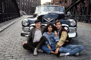 Mit Hilfe von Schorsch (Klaus Herm, l) und Susi (Maria Ketikidou) hat Pit (Ralf Komorr) einen alten Cadillac wieder fahrbereit gemacht. Mit diesem „Wägelchen“ will der Botenjunge seiner großen Liebe am Caro imponieren, die Sängerin in einer Band ist
Kann für beide Teile verwendet werden