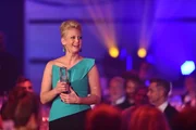 Barbara Schöneberger hält den Preis mit beiden Händen fest. Sie strahl Freude aus. Im Hintergrund das Publikum.