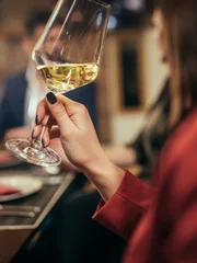 Group of people, men and women, sitting in restaurant together, woman holding wineglass.