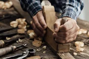 Carpenter working in his workshop, he is smoothing a wooden board using a planer