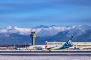 Alaska Airlines plane landing with mountains and control tower in background