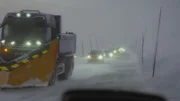 A snow plower is spear heading a convoy over the mountain.