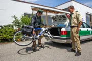 Staller (Helmfried von Lüttichau, links) versucht sein kaputtes Rad in den Streifenwagen zu laden, damit sie es heimlich entsorgen können. Hubert (Christian Tramitz) schaut ihm dabei gelangweilt zu.