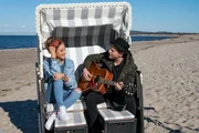 Johannes Oerding spielt Moderatorin Laura Dahm während des Interviews am Strand einen Song auf der Gitarre vor.