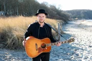 Johannes Oerding steht am Strand mit seiner Gitarre.