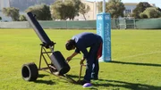 Kevin and Grant venture out to a football field to properly test the distance it shoots footballs. Kevin is about to send off another football while Grant waits in anticipation on the other side of the field.