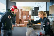 Franzi (Rhea Harder-Vennewald, r.) möchte vom Pizzaboten (Simon Gosejohann, l.) wissen, ob er die Frau auf dem Foto erkennt, was sich bei dessen Zustand als schwierig erweist.