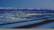 Aerial wide shot of the airport, runways and Anchorage lights and mountains in the distance, in the early evening