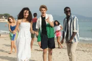 Ines (Eubha Akilade, l.), Jeff (Castle Rock Peters, M.) und Isaac (Terique Jarrett, r.) beobachten amüsiert, wie die eben noch frustrierte Lena ausgelassen mit einem Unbekannten am Strand tanzt.