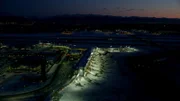 Aerial view of the airport terminals and apron at sunset / night, with the lights of Anchorage in the distance, with the mountains