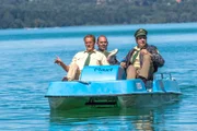 Hubert (Christian Tramitz, links) und Staller (Helmfried von Lüttichau, rechts) sitzen in einem Tretboot und fahren auf den See hinaus. Yazid (Hannes Ringelstetter) sitzt hinter ihnen in Tauchermontur. Er soll für Hubert und Staller testen, ob man mit einem Schlittschuh unter Wasser an einer Boje hängen bleiben kann.