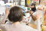 Masked thief pointing a gun to sales woman in a store