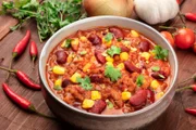 Chili con carne, a traditional Mexican dish with red beans, cilantro leaves, ground meat, and chili peppers, a closeup with ingredients