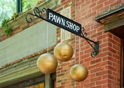 A sign for a pawn shop with three hanging gold spheres. A wrought iron bracket is attached to a brick store front