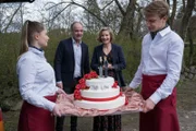 Oskar Schütz (Marek Erhardt, 2.v.l.) und Lena Testorp (Anna von Haebler, 2.v.r.) lassen ihr Hochzeitsgeschenk in Form der Hochzeitstorte von der Cateringfirma (Komparsen) zu den Feiernden bringen.