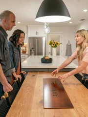 As seen on HGTV’s Help! I Wrecked My House, the Traficantes react as host Jasmine Roth reveals their new dining room featuring a custom-made oak table with a steel plate bearing the family mantra "Explore".(Reveal). .