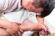 Man on bed with pillow embrace foot with painful swollen gout inflammation