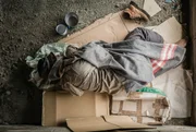 Old homeless man wearing sweater and blanket sleeping on cardboard