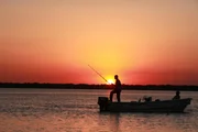 Jeremy fishing from boat, silhouetted against sunset. Parana River South of Bella Vista.