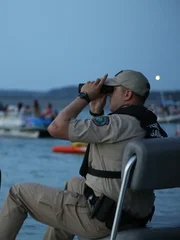 Warden McGinley on boat looking through binoculars.